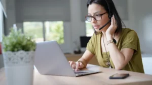 Mulher usando VoIP em home office com fone e computador.